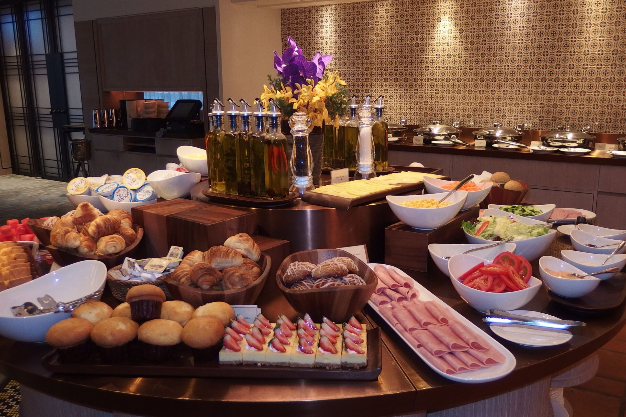 Hotel breakfast buffet display with fresh fruit, pastries, and hot dishes in upscale restaurant setting