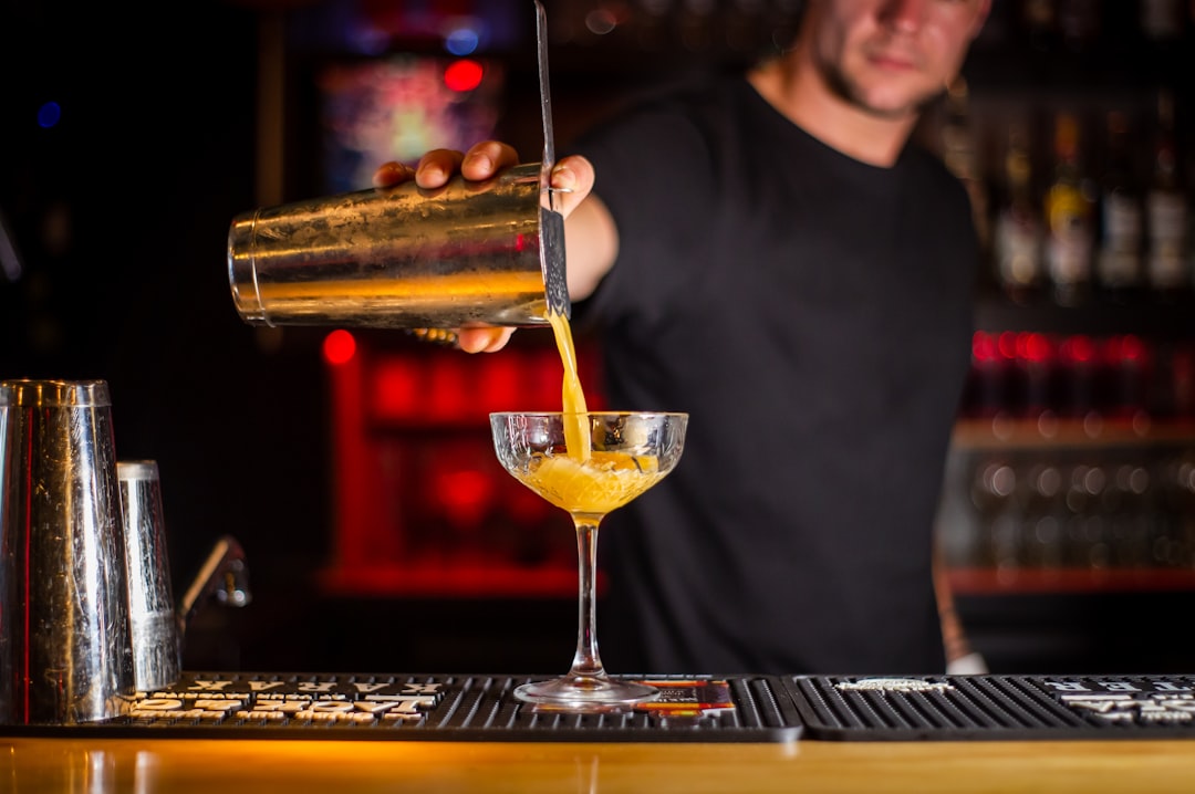 A smiling bartender pours a classic Aperol spritz cocktail into a large wine glass filled with ice and an orange garnish.