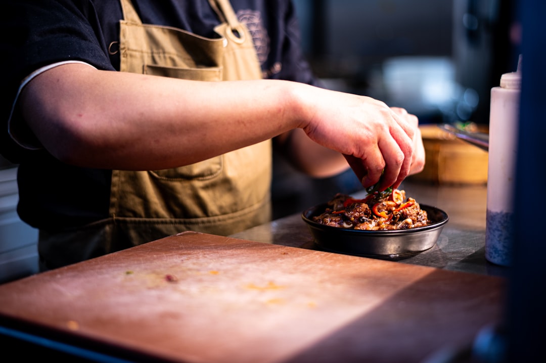 A chef carefully assembles a balanced grain bowl with layered grains, vegetables, and fresh herbs on a wooden counter