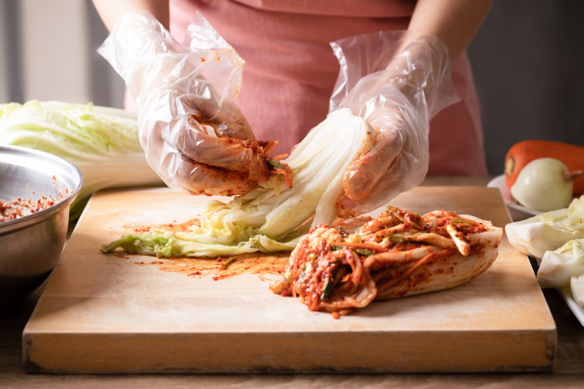 A woman prepares kimchi by hand, layering cabbage in a traditional crock, demonstrating the ancient craft behind this dish.