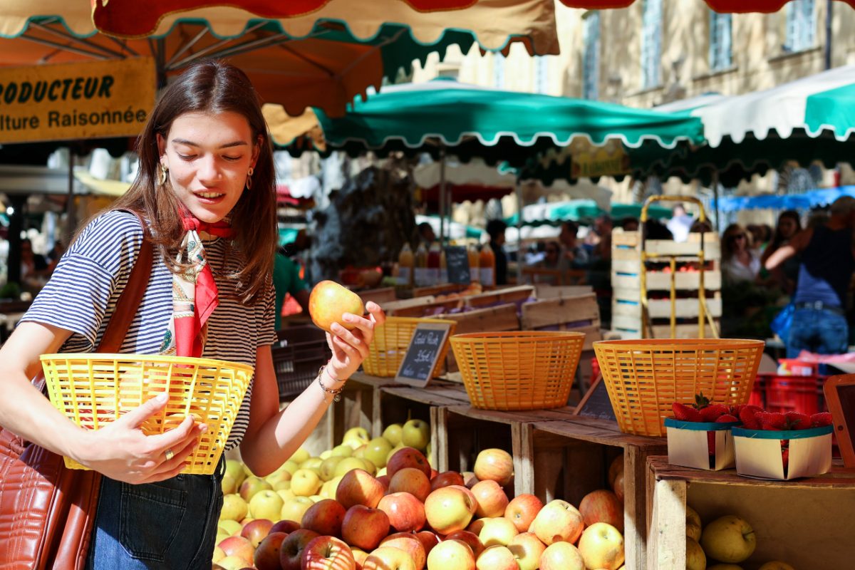 A woman carefully arranging ripe stone fruit at a summer farmers market, selecting the best peaches and plums for storage