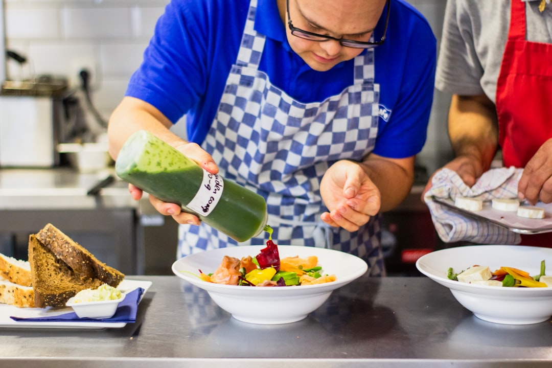 A chef carefully pouring chilled soups into a white bowl in a professional kitchen
