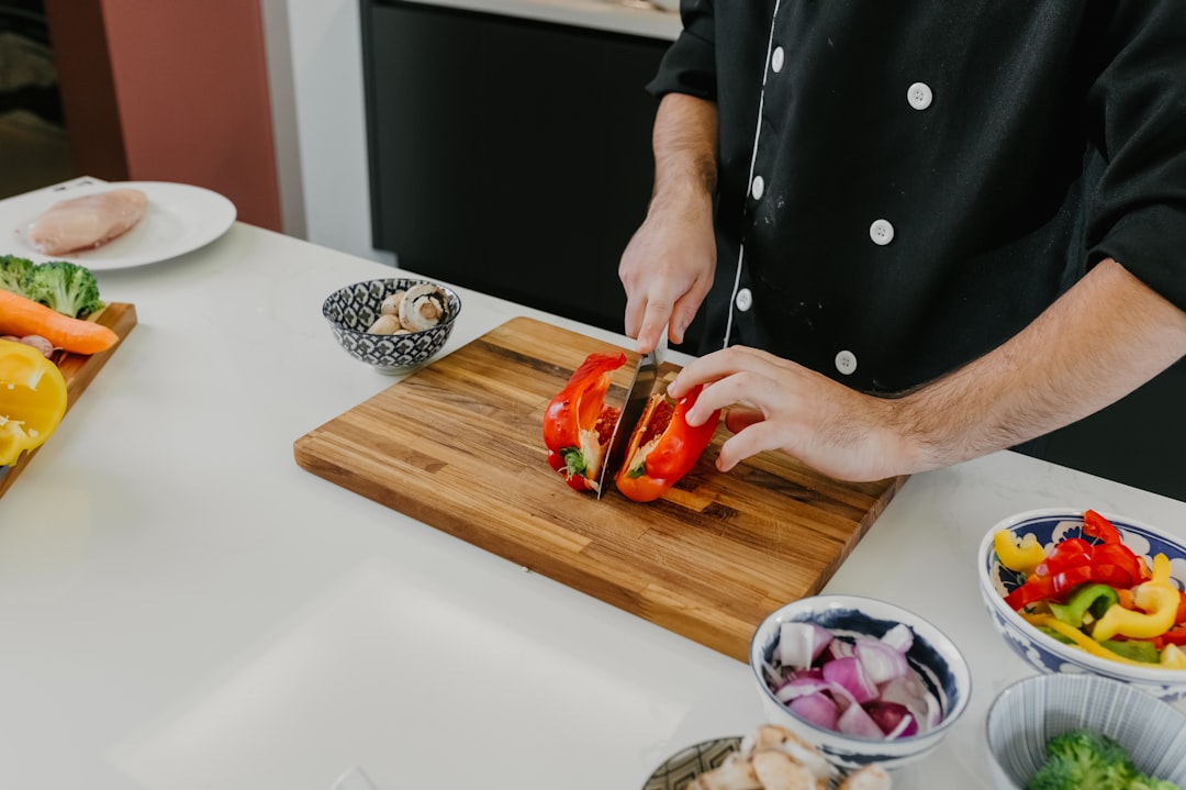 A chef demonstrating knife skills while slicing fresh summer tomatoes on a wooden cutting board