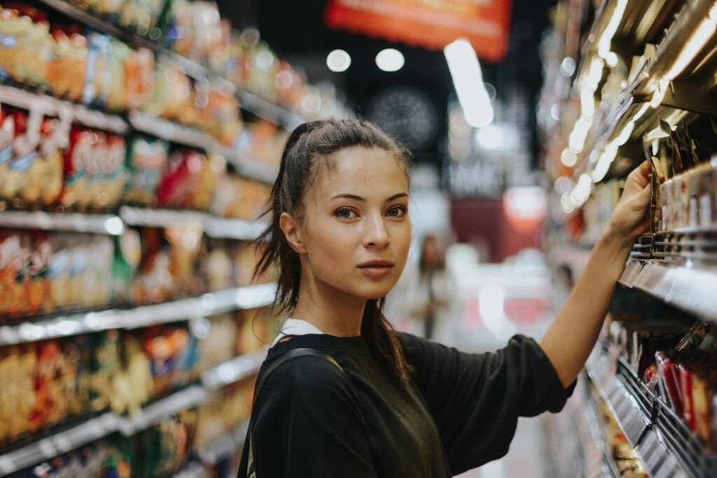 Woman shopping in a supermarket aisle, reaching to grab an item from the shelf.