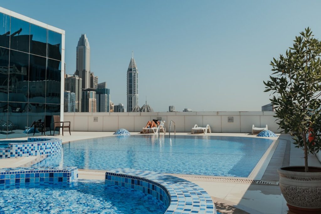Rooftop swimming pool with blue mosaic tiles and a city skyline in the background under a clear blue sky