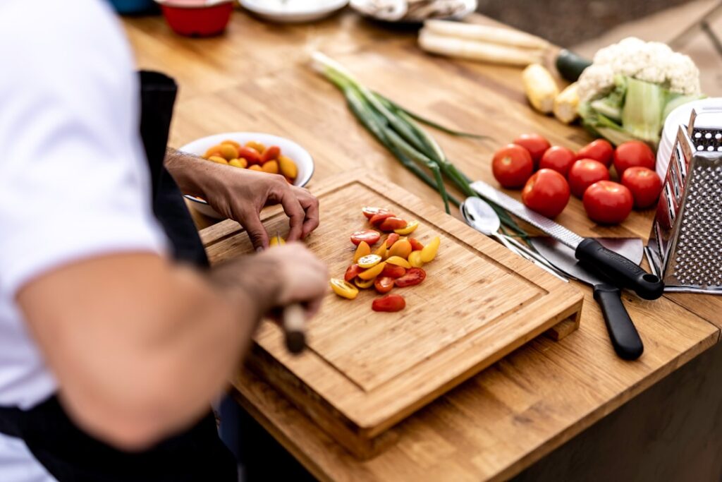 A person chopping multicolored cherry tomatoes on a wooden cutting board in a kitchen.