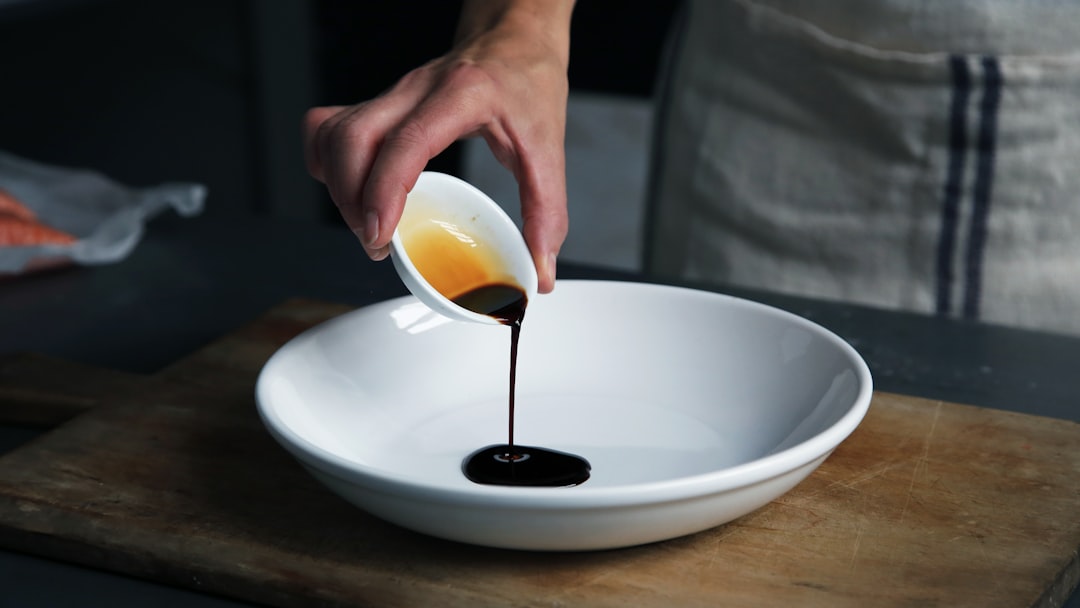 A chef carefully drizzling aged vinegar over a finished plate in a professional kitchen