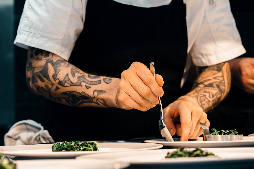 A professional chef adjusting salt acid and seasoning in a large pot in a busy restaurant kitchen