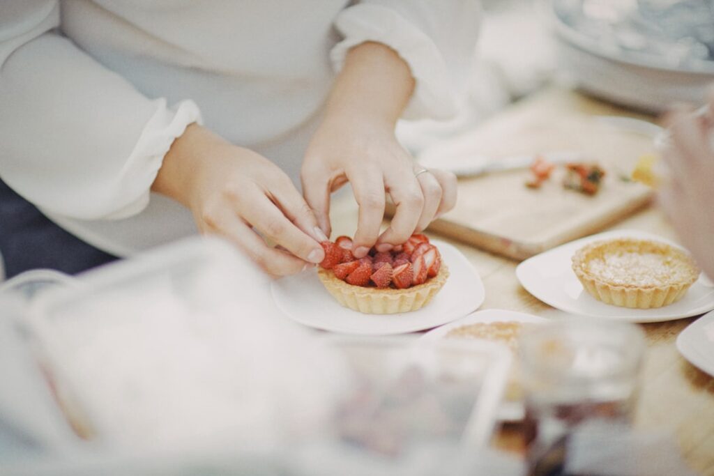 Close-up of hands decorating a strawberry tart with sliced berries on a white plate