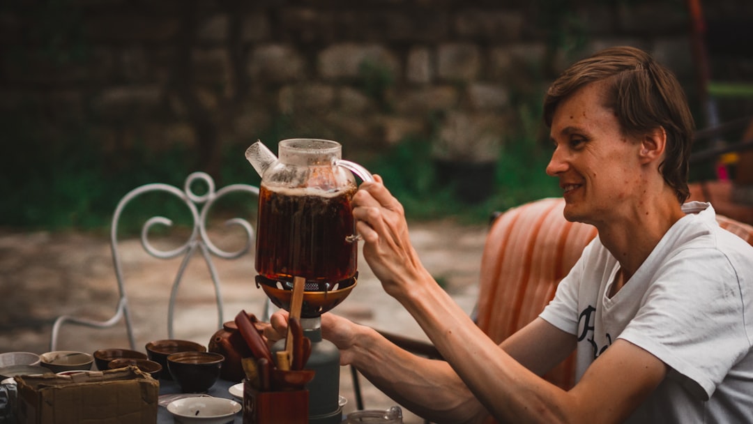 A woman carefully pouring cold brew tea from a glass jar into a cup on a wooden kitchen counter
