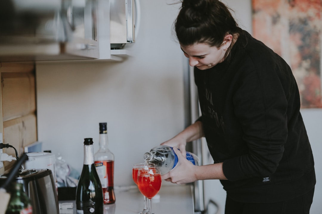A woman carefully pouring a glass of fermented drinks at a bright kitchen counter, surrounded by seasonal autumn produce