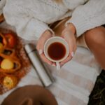 A woman cradles a ceramic mug of warm spiced drinks beside autumn leaves, showing the seasonal comfort of drink traditions.